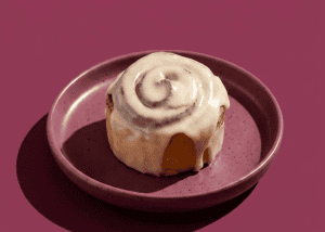 Rollo de canela clásico con glaseado en plato rosa sobre fondo rosa.