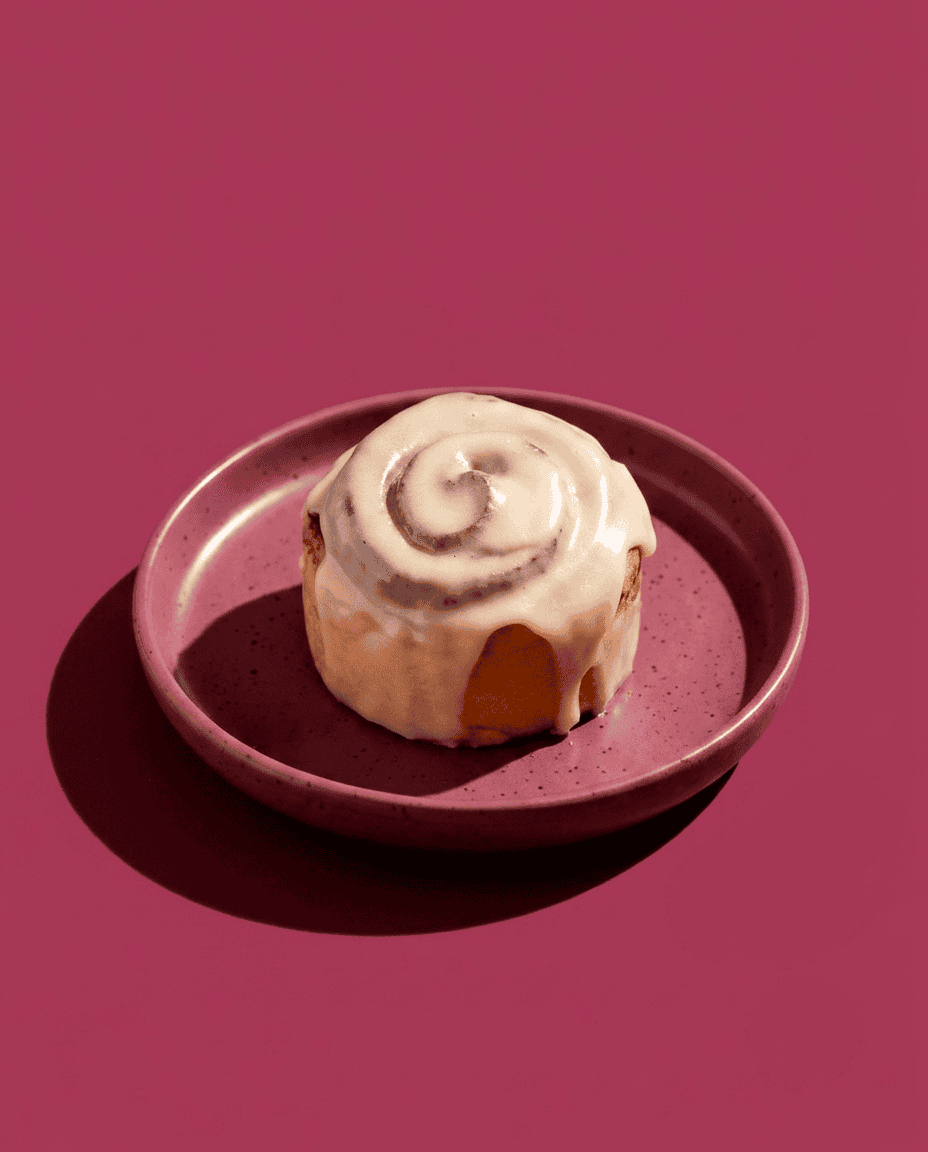 Classic Cinnamon Roll Candela Rolls Studio 7 Rollo de canela clásico con glaseado en plato rosa sobre fondo rosa.