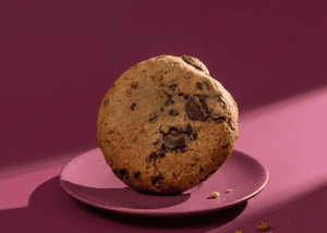 Galleta con chispas de chocolate en plato rosa sobre fondo rosa oscuro.