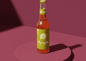Botella de zumo Fritz-Spritz en fondo rosa, producto saludable y refrescante.