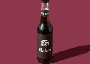 Botella de Fritz-Kola en fondo rosa con sombra.