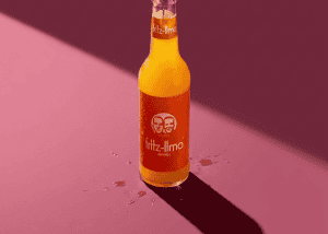 Botella de Fritz-Limo de naranja en fondo rosa con sombra larga.