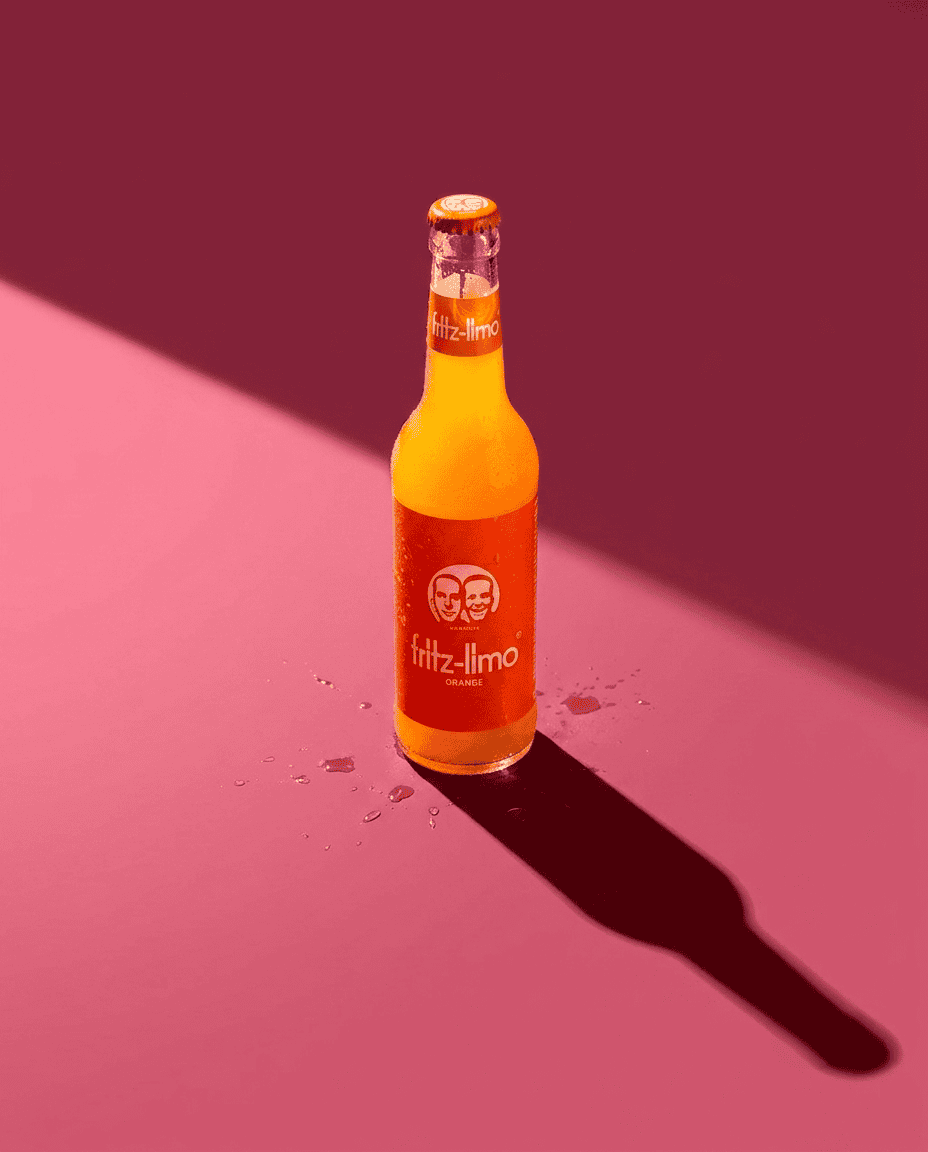 Fritz Limo Candela Rolls Studio 1 Botella de Fritz-Limo de naranja en fondo rosa con sombra larga.