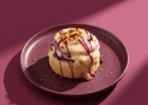 Helado de vainilla con salsa de fresa y crumble en plato rosa.