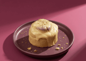 Dulce de leche con topping de pistacho en plato gris sobre fondo rosa.